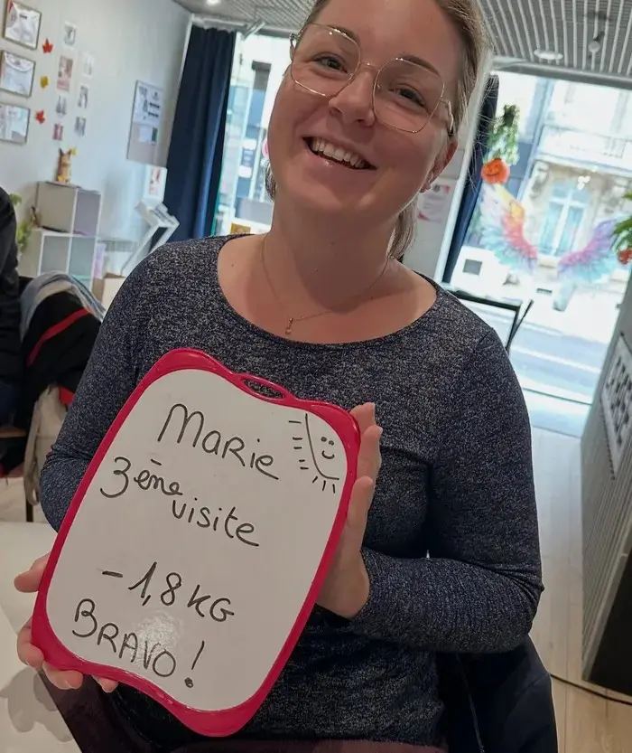 Marie avec son ardoise : 3e visite : −1,8 kg. Aujourd'hui, elle en est à −2,1 kg.