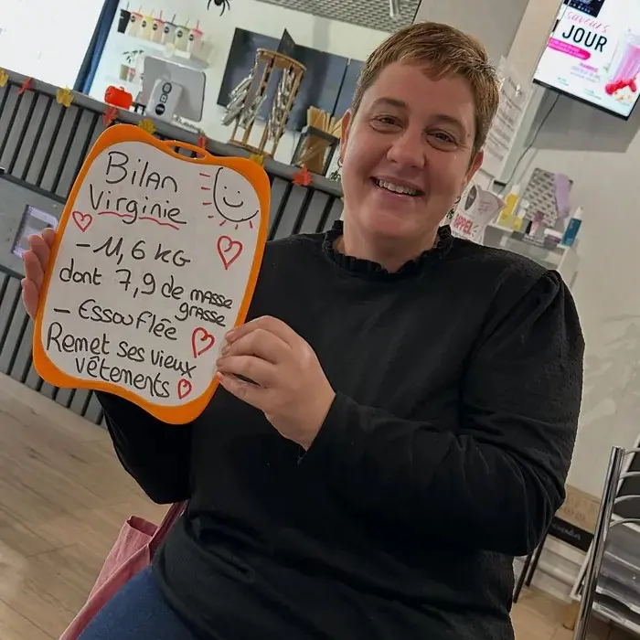 Virginie avec son ardoise : Bilan : −11,6 kg, dont 7,9 kg de masse grasse. Elle remet ses vieux vêtements.