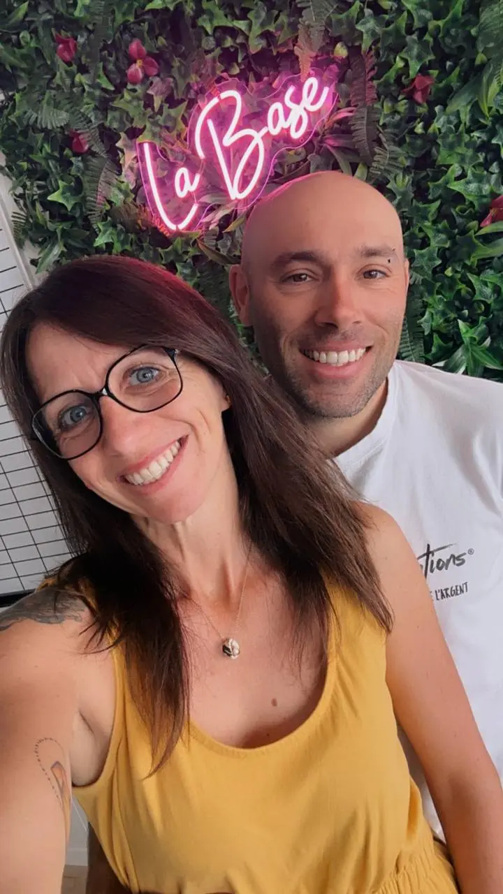 Mélanie et Thomas, souriants devant le mur végétal et l'enseigne lumineuse La Base.